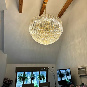 Oversized tiered crystal chandelier hanging from a vaulted ceiling with exposed wood beams in a two-story living room