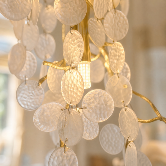 A multi-tiered cascading crystal chandelier with a gold frame hangs in a grand foyer with a curved staircase.